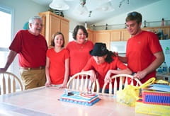Carol blowing out birthday candles at a dining room table while her family looks on