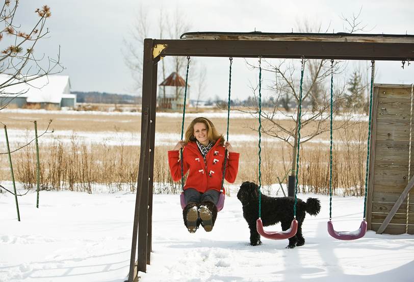 Coree in snow swinging on swing with her dog in background