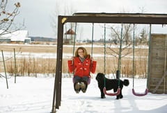 Coree H in snow swinging on swing with her dog in background