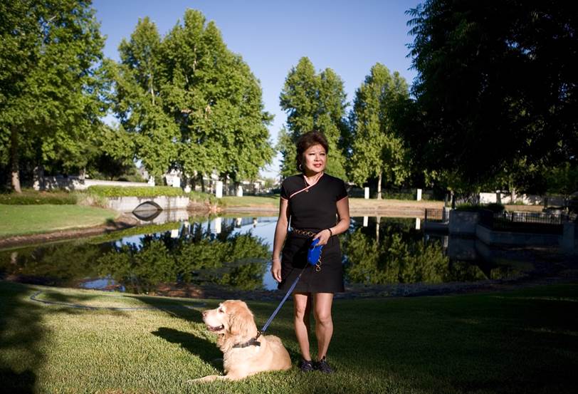Katherine Y standing in a park in front of a pond holding a leash with a golden retriever resting in front of her