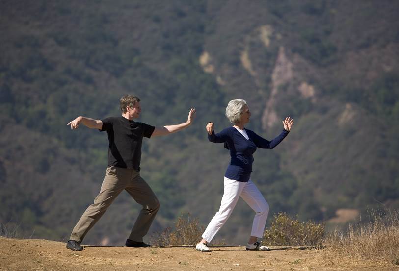 Image of Laurie L and partner doing Tai Chi with forested hill in background