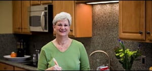 Linda P. standing in kitchen with the words Linda had a mammogram exactly one year before her diagnosis that showed nothing