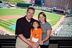 Mike and two girls in upper deck stadium with baseball field in the background