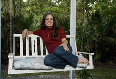 Susie R. sitting on white porch swing and trees in background